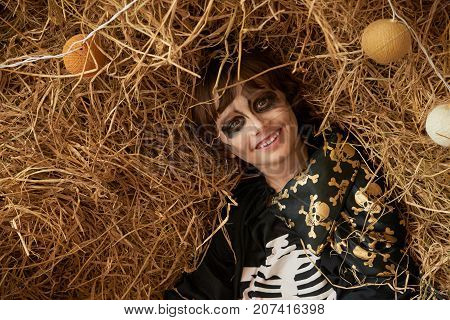 Smiling boy with scary Halloween make-up lying in hay