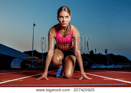 Portrait of beautiful woman ready to start running. Female athlete sprinter doing a fast sprint for competition on red lane at an outdoor field stadium.