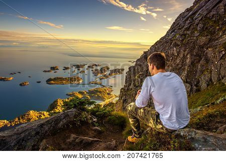 Male hiker on the trail to mount Festvagtinden with views over the village of Henningsvaer. Henningsvaer is a fishing village located on several small islands in the Lofoten archipelago in Norway.