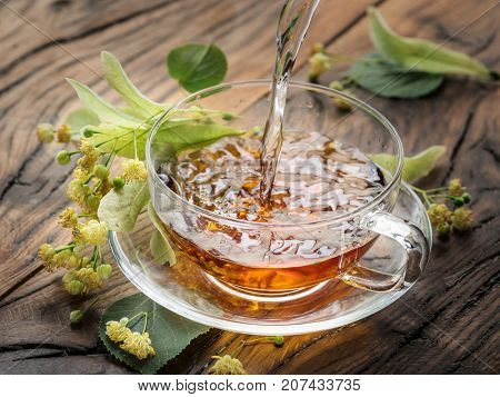 Cup of linden tea and lime flowers on the wooden table.