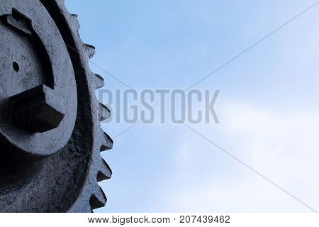 The old big black cog wheel against the blue sky.