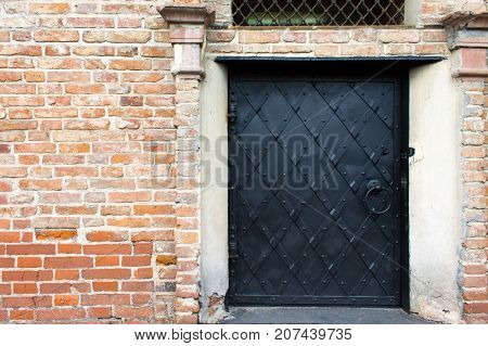 Black iron door with riveted stripes in an old red brick wall.
