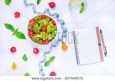 Top View Salad Bowl With Cherry Tomatoes, Broccoli, Measuring Tape And Diet Book On The White Wooden