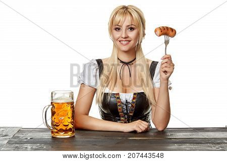 Young bavarian woman in dirndl sitting at table with beer on white background. Oktoberfest