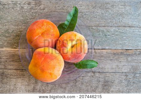 Three ripe peaches with green leaves in a plastic plate on the old wooden background