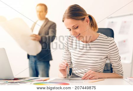 Talent and creativity. Delighted pleasant talented woman holding a pair of compasses and doing a drawing while working on a project