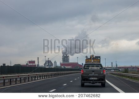 SEBES ROMANIA - SEPTEMBER 23 2017: Truck driving on a Romanian motorway near the road of Sebes a highly polluting wood processing factory can be seen in the background