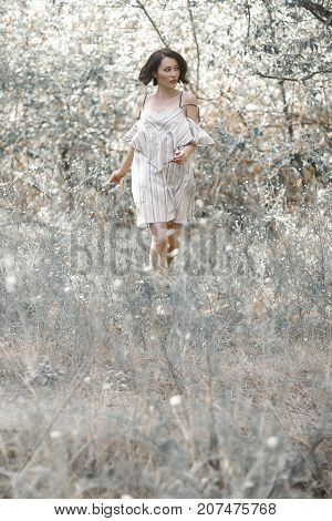 fashion styling girl is emotional. she is dressed in white with black stripes dress.forest with trees. girl in dinamic. model is running or jumping. woman in wonderland