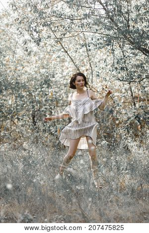 fashion styling girl is emotional. she is dressed in white with black stripes dress.forest with trees. girl in dinamic. model is running or jumping. woman in wonderland