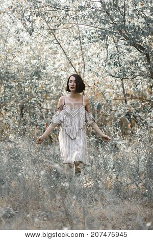 fashion styling girl is emotional. she is dressed in white with black stripes dress.forest with trees. girl in dinamic. model is running or jumping. woman in wonderland