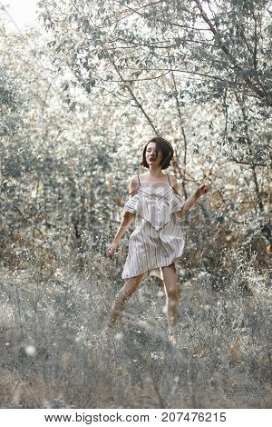 fashion styling girl is emotional. she is dressed in white with black stripes dress.forest with trees. girl in dinamic. model is running or jumping. woman in wonderland