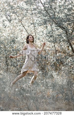 fashion styling girl is emotional. she is dressed in white with black stripes dress.forest with trees. girl in dinamic. model is running or jumping. woman in wonderland