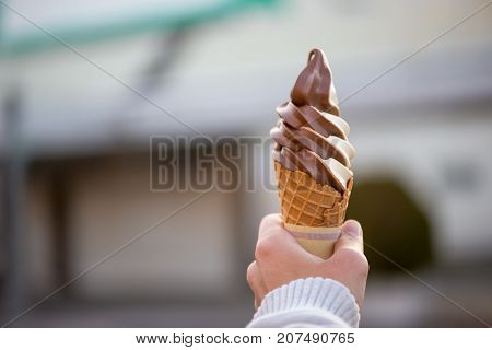 Close-up detail of a chocolate vanilla twist soft serve in a crispy homemade waffle cone with blurred background and sweater hands. Nobeoka Japan. Travel and food concept.