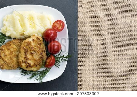 Two juicy fried meat patties on a white plate with cherry tomatoes and mashed potatoes.