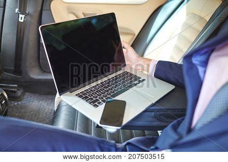 Close-up of a young businessman who uses a laptop to work in the backseat of a car.