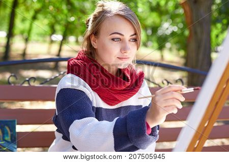 The femae artist paints a picture in the sunny day in a good mood. Young woman drawing a picture in autumn park.