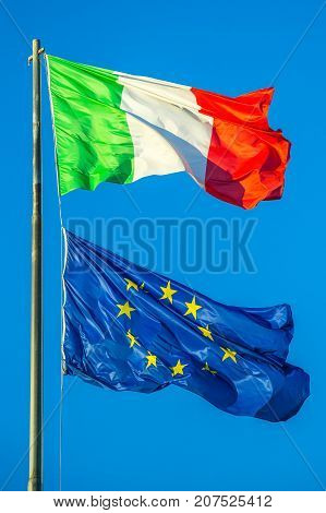 Flags of Italy and Europe waving in the blue sky background. Concept for financial treated, unique currency and financial bond