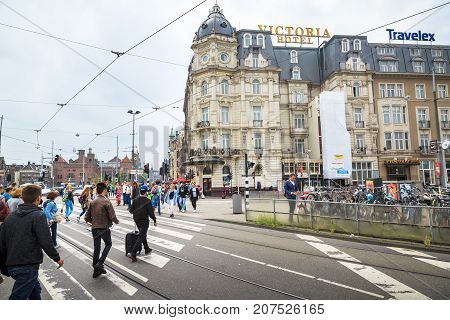 AMSTERDAM NETHERLANDS - JUNE 21 2016: Wide picture of the busy Damrak Street with many people a bicycle parking and hotels in a cloudy day. Amsterdam Netherlands.