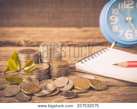 Vintage baby tree with coins red pencil noot book and alarm clock on old wooden background. Business financce and saving money concpt.