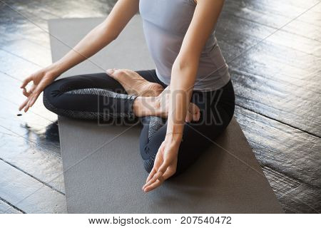 Close up of sporty young woman practicing yoga, sitting in Lotus exercise, Padmasana pose with mudra, working out wearing sportswear, studio floor background. Wellbeing and wellness concept