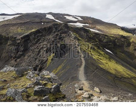 The path along the black crest of a volcano overgrown with bright green moss Iceland