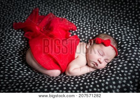 Sleeping pretty newborn in red dress and a small ribbon on his head.