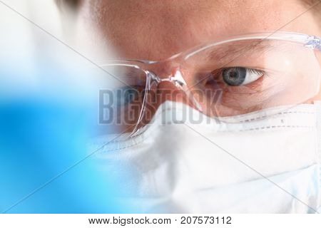 A portrait of a young surgeon chemist's doctor looks at a container with a blue liquid and a mask is fought with viruses and a vaccine for vaccines against diseases