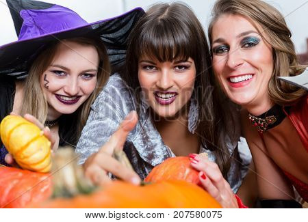 Three young and beautiful women wearing funny party costumes while acting as witches joining their malicious forces at Halloween