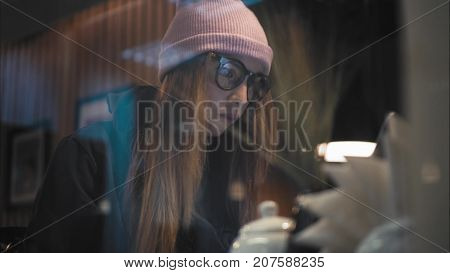 A stylish hipster woman sitting in cafe and working with laptop. View through the window