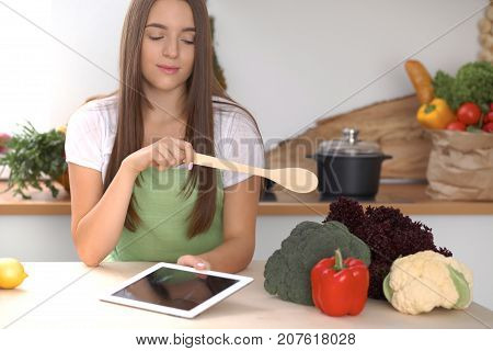Young  woman is making online shopping by tablet computer and credit card. Housewife found new recipe for  cooking in a kitchen.