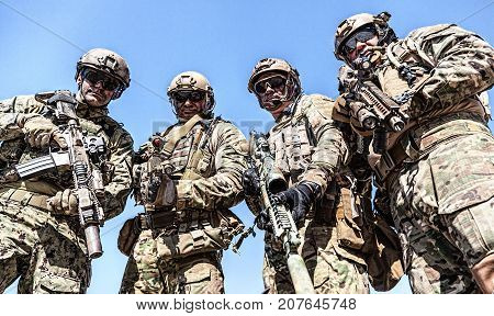 Half length low angle location shot of special forces soldiers in field uniforms with weapons, portrait on blue sky background