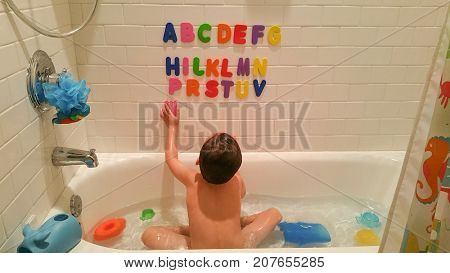 Young Boy Having Fun With The Alphabet On Wall At Bath Time.