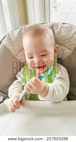 Adorable Chinese and Caucasian Baby Boy Playing With His Spoon Sitting in High Chair.