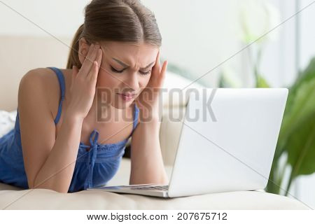 Computer headache concept, young woman suffering from strong chronic headache, touching temples with eyes closed, stressed student feeling sudden pain attack after long using laptop for study at home