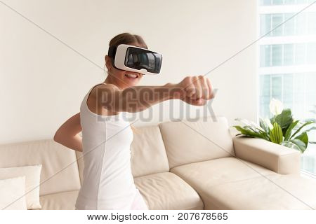 Young teen gamer wearing augmented reality glasses standing in boxing stance playing action simulator game mobile app, female player fighting with fist in VR headset, virtual training new technology