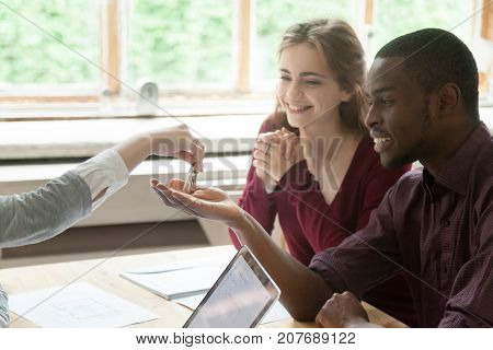 Real estate agent handing new house keys to happy multiethnic couple. African american man and his wife are excited to buy new house or apartment. Young interracial couple bought first home together.