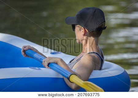 Adult woman readies the paddle wile on an inflatable craft in the water near sunset