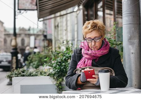 Adult pretty woman browsing smartphone in outside cafe.