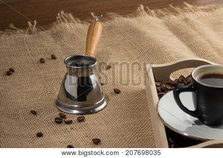 Coffee gezve. Coffee grains and cup of coffee in wooden box. Coffee gezve and box on the sackcloth background. Brown image