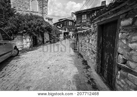 NESEBAR BULGARIA - AUGUST 21 2017: A typical residential building and a street with tourists in the old town. Nesebar is an ancient city and one of the major seaside resorts on the Bulgarian Black Sea Coast. Black and white.