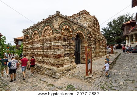 NESEBAR BULGARIA - AUGUST 21 2017: Church of the Holy Archangels Michael and Gabriel (built between the 13th and 14th centuries) and a street with tourists in the old town.
