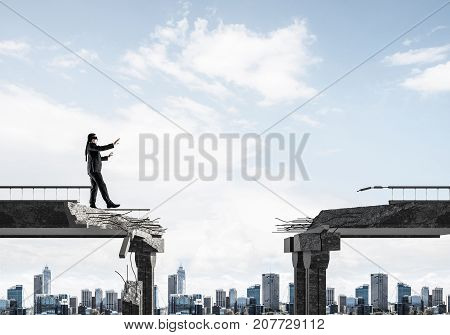 Businessman walking blindfolded on concrete bridge with huge gap as symbol of hidden threats and risks. Cityscape view on background. 3D rendering.