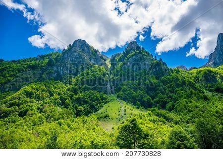 Scenic Green Meadow On The Background Of High Peaked Rocks.