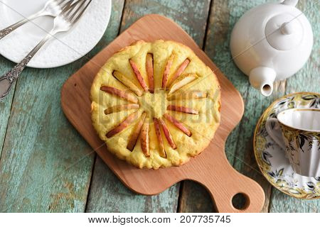 Homemade delicious rustic cake with apple slices looking like sun rays with teaware on shabby wooden blue table above view