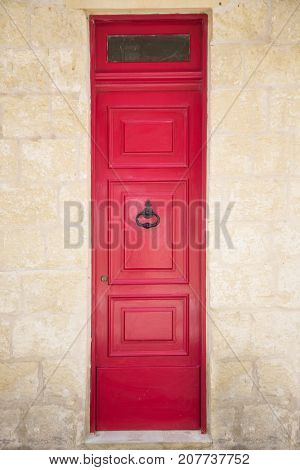Red painted old wooden door with black iron handle in medieval city street