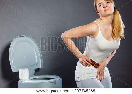 Bellyache constipation or food poisoning. Woman suffering from strong abdominal pain holding medical tablets activated carbon in hand paper on toilet in the background