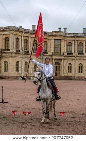 Gatchina St. Petersburg Russia - September 30 2017: Horse show of Cossacks on the parade ground of the Gatchina Palace. Cossack in a white shirt on a horse with a red flag.