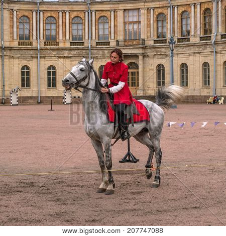 Gatchina St. Petersburg Russia - September 30 2017: Horse show of Cossacks on the parade ground of the Gatchina Palace. A Cossack girl in a red outfit on a white horse.