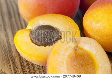 A Bunch Of Apricots Lying On An Old Wooden Table. One Apricot Is Divided By A Knife Into Two Halves,