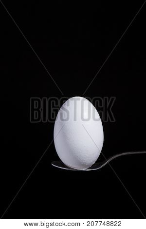 white egg on a spoon on a black background